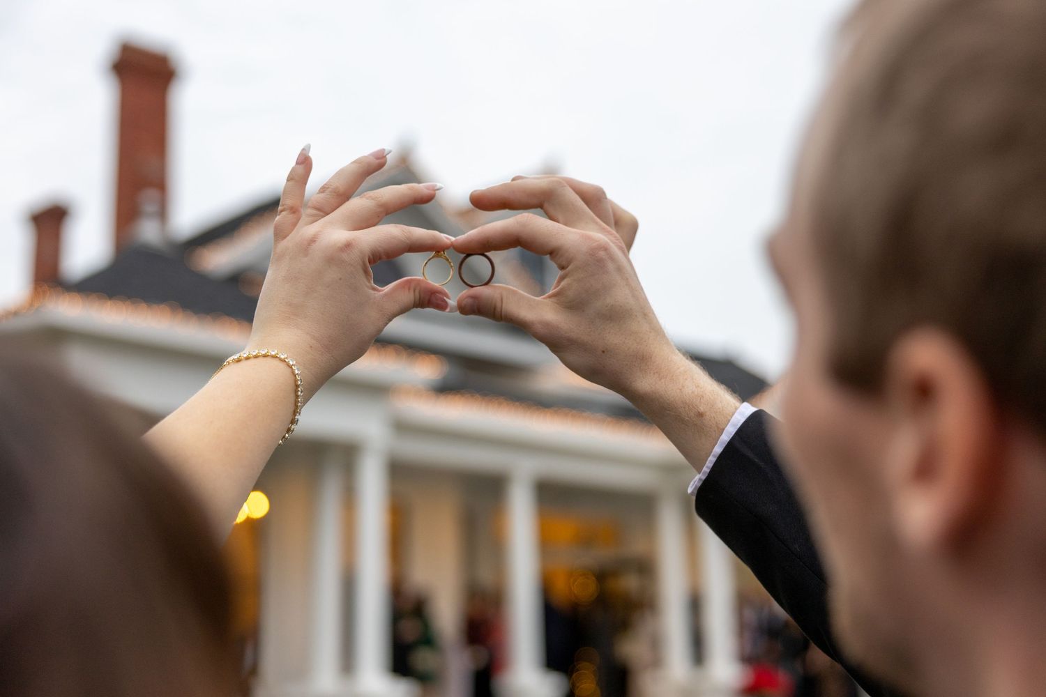 A couple holds up their rings with the House on Barber Mill in the background.
