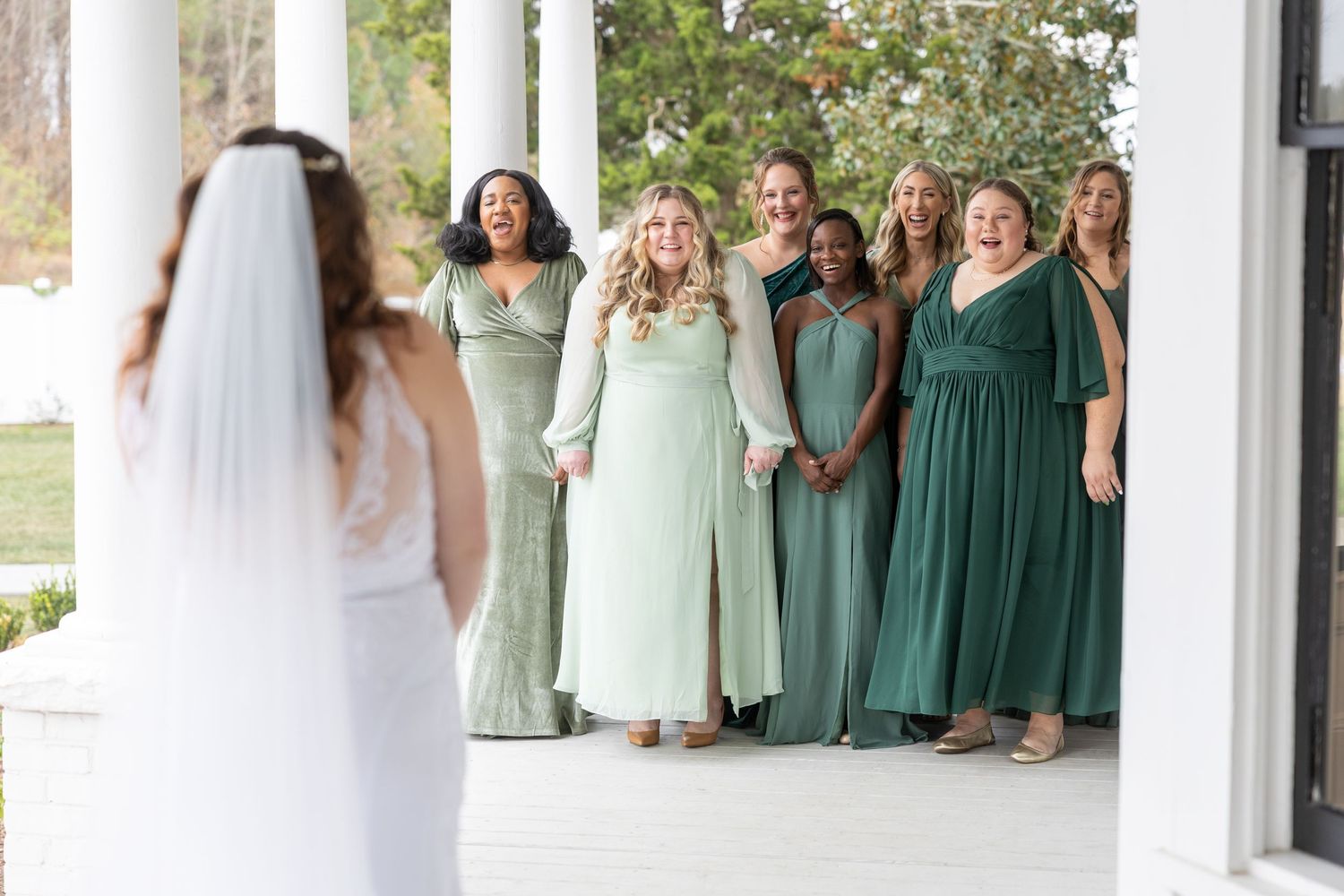 A bride looks at her bridesmaids in green shaded dresses in her Clayton, NC wedding.
