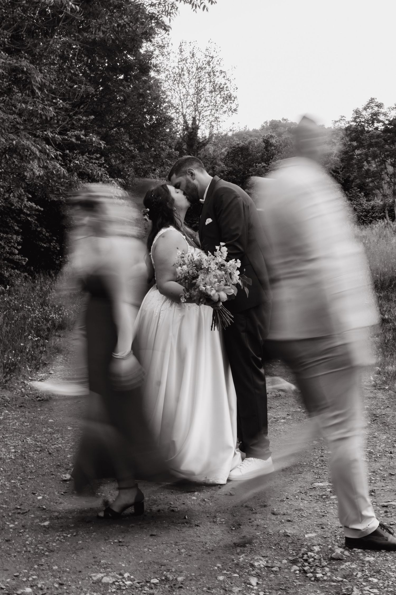 Artistic black and white wedding photo with motion blur of guests walking past the newlyweds.