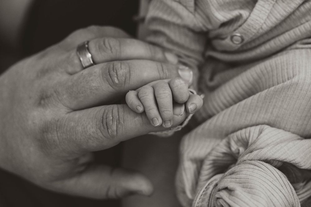 Black and white photo of a newborn baby holding a parent's finger with a wedding ring.