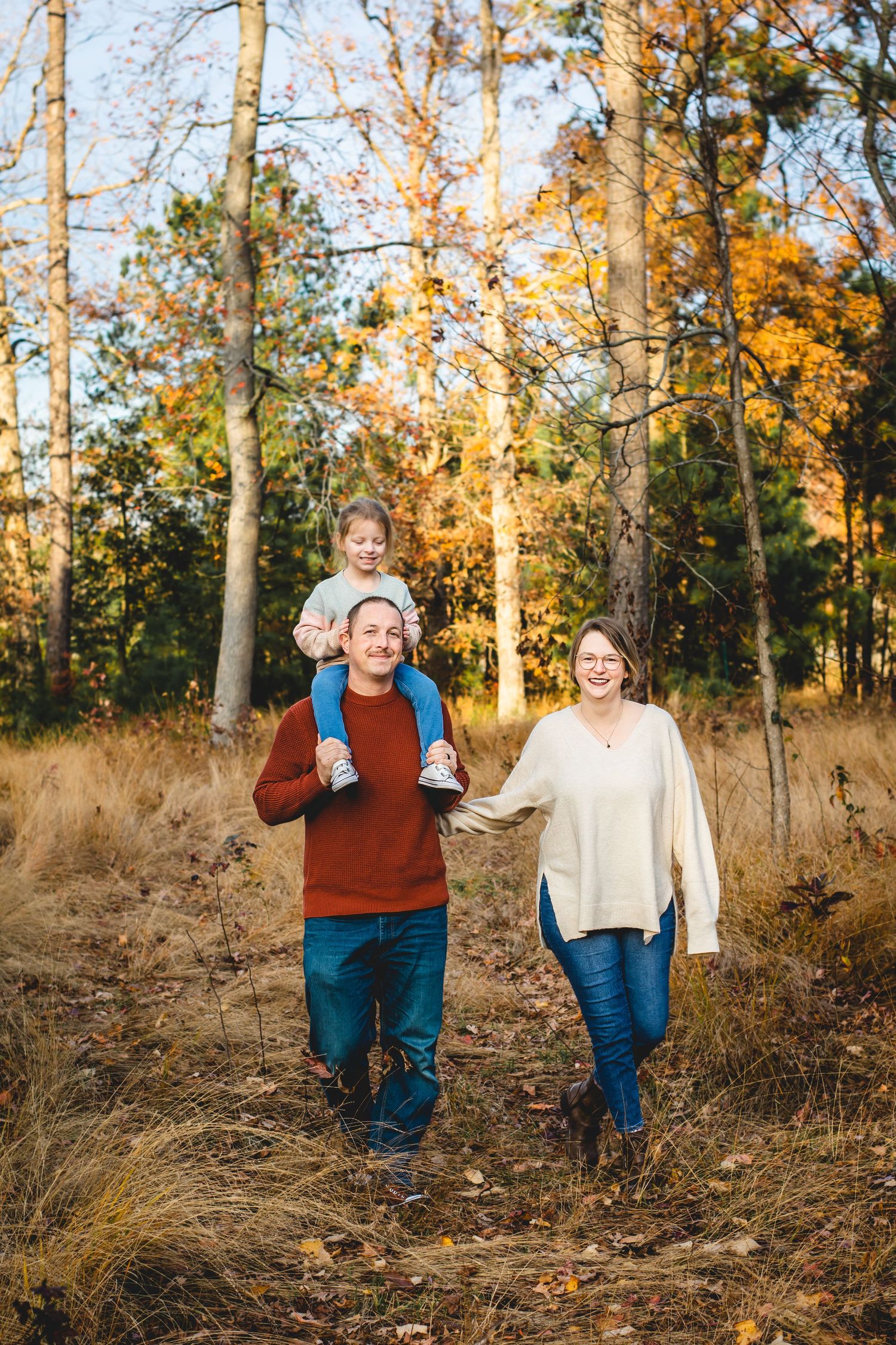 Family walking through autumn woods during golden hour photoshoot.