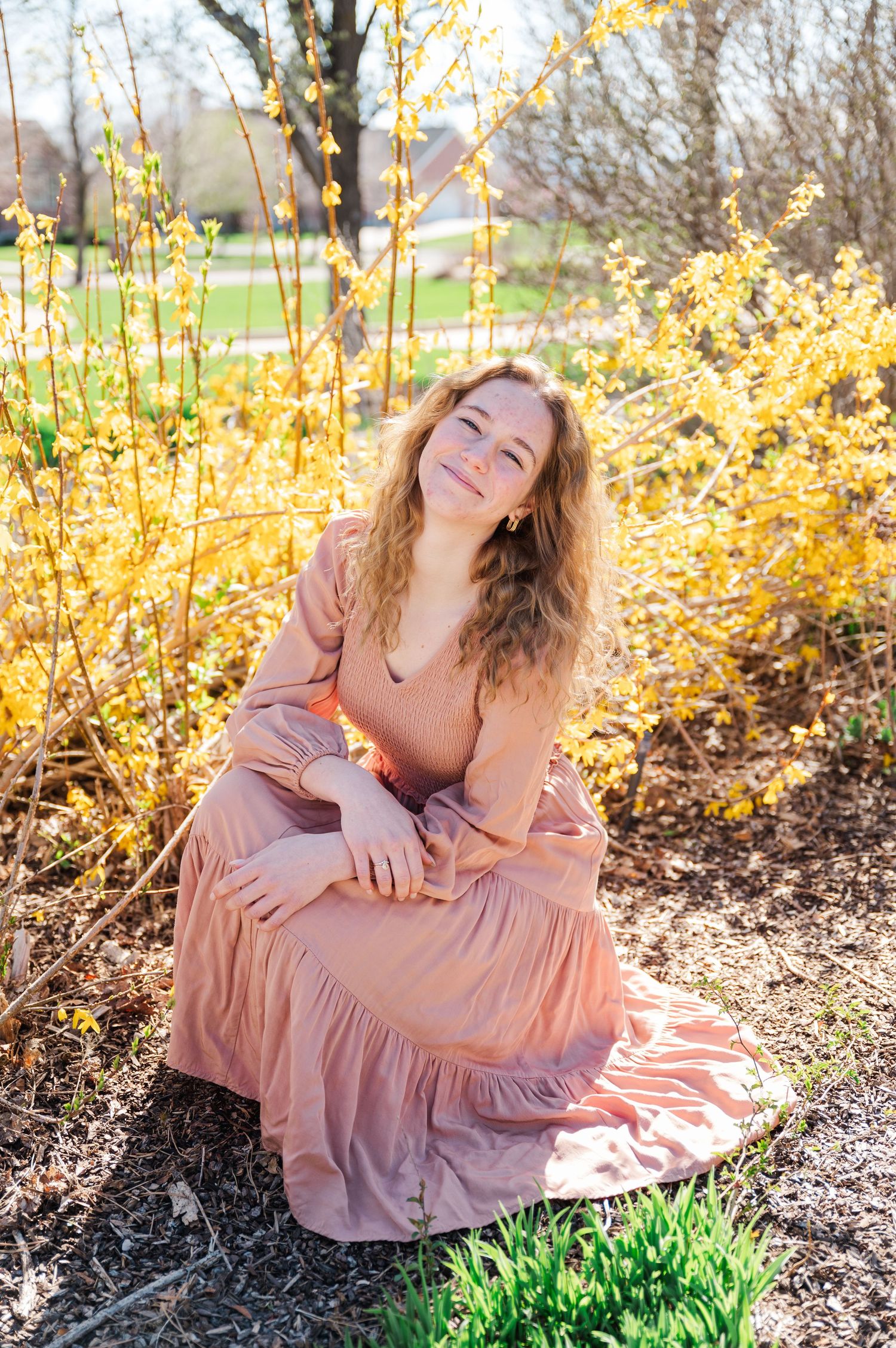 Woman in pink dress sitting among blooming forsythia bushes in spring garden.