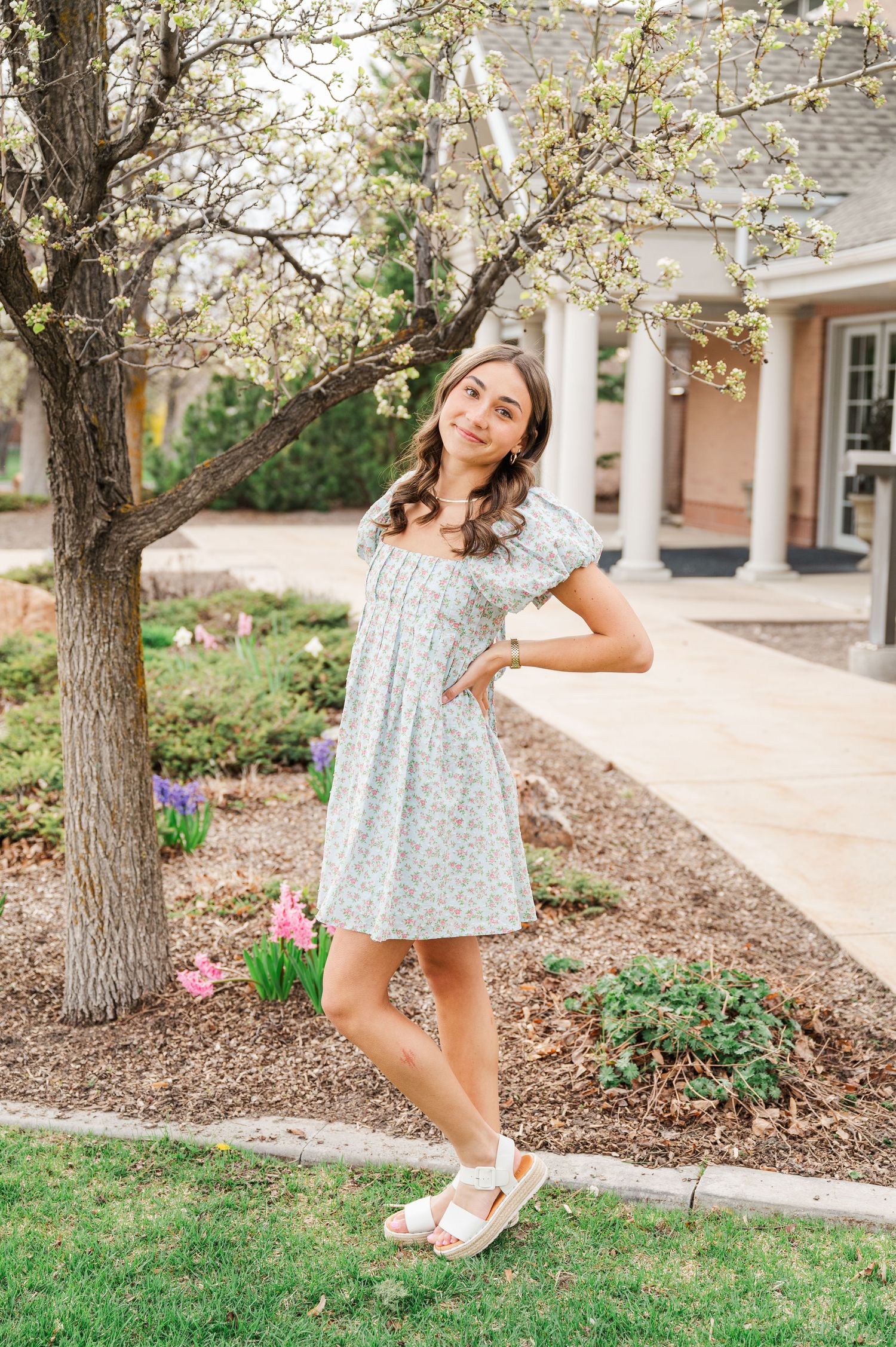 Woman in spring dress poses by blooming tree and colonial style building.