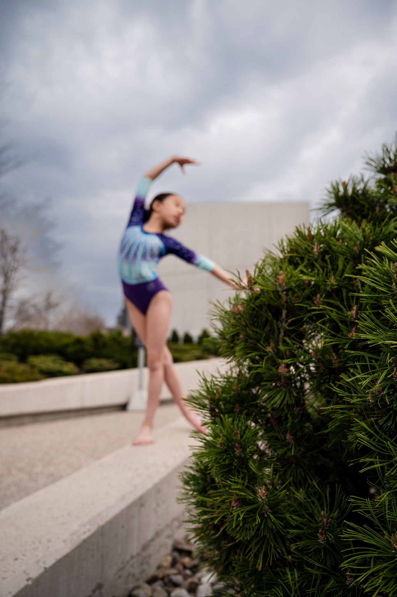 Dance pose performed near landscaped bushes against modern architecture.