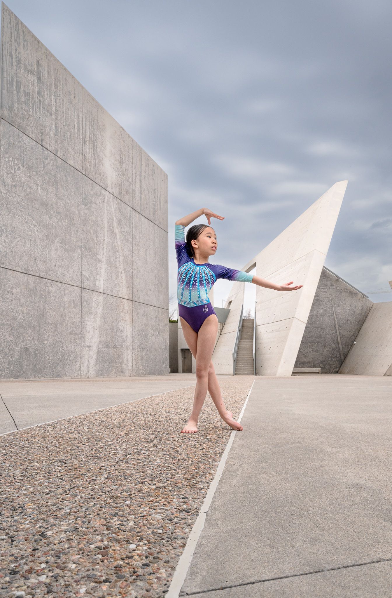 Young dancer strikes graceful pose against geometric concrete architecture.