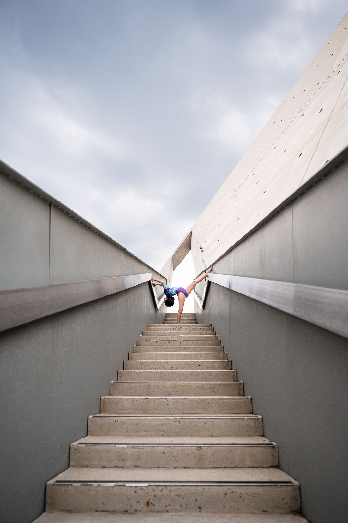 Steep concrete staircase leading upward between angular walls under cloudy sky.