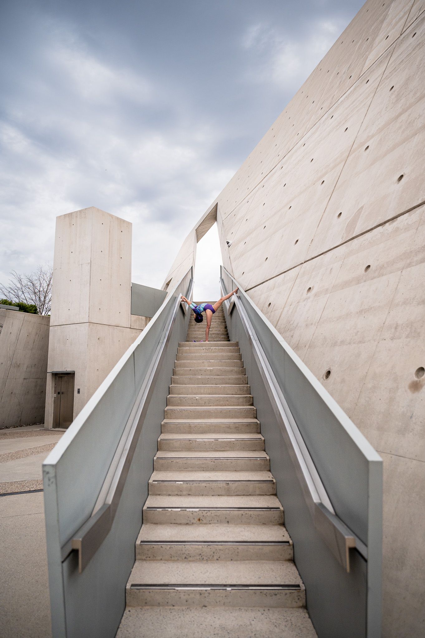 Modern concrete stairway with metal handrails leading upward under cloudy sky.