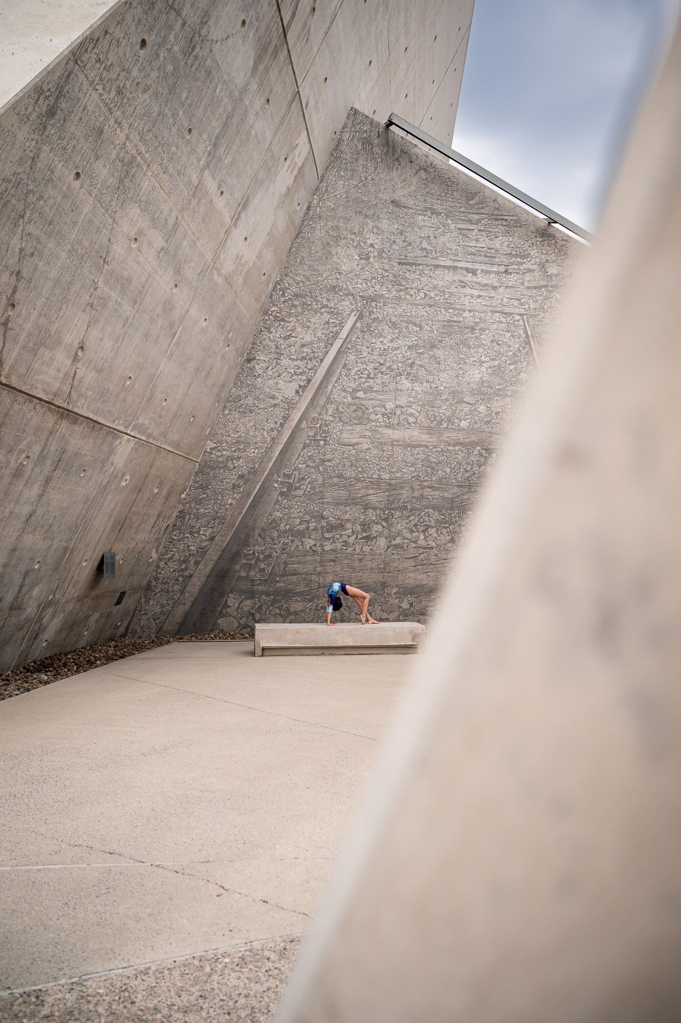 Gymnast performs on concrete ledge against angular architectural walls.