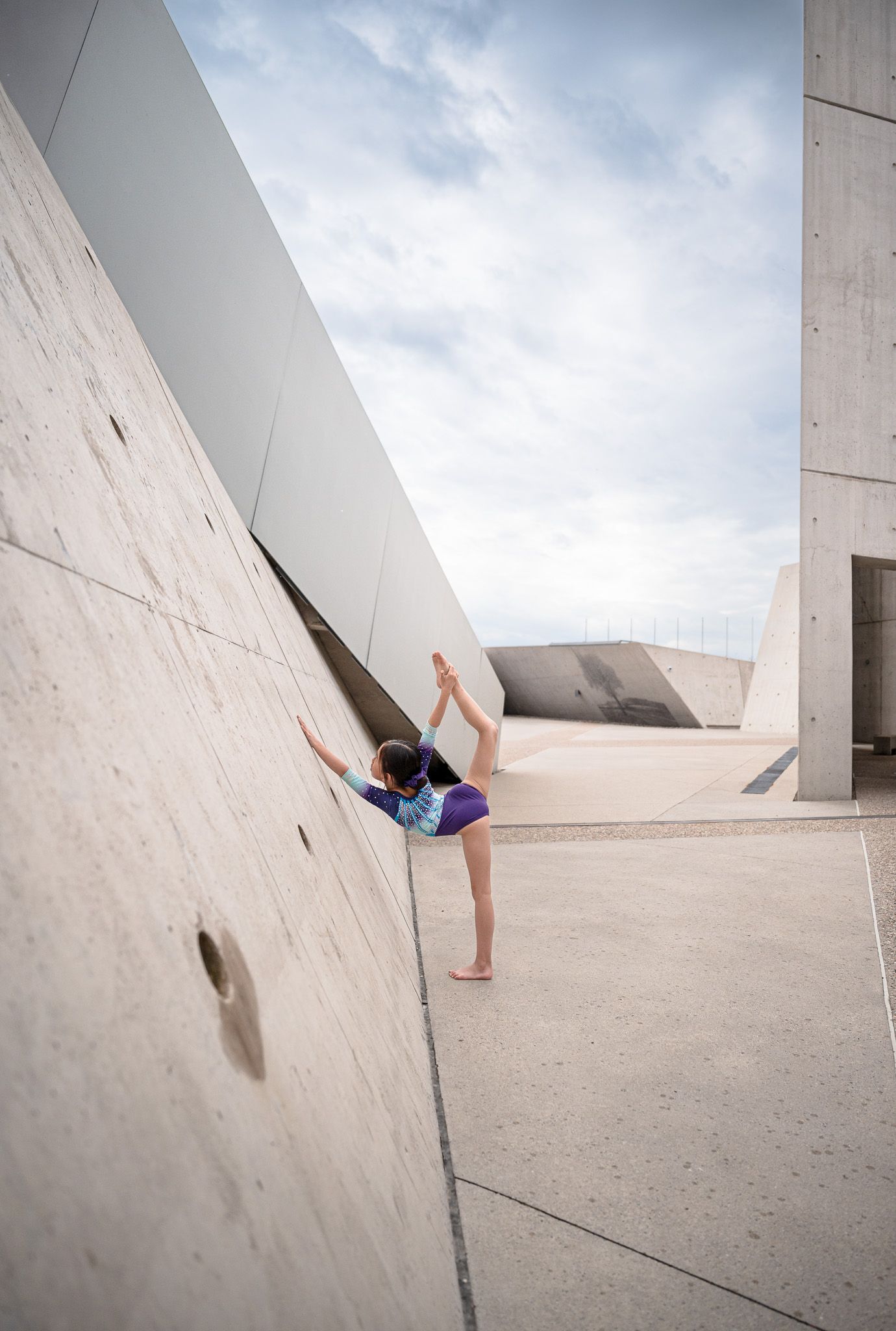 Gymnast executing split pose against angular concrete architecture.