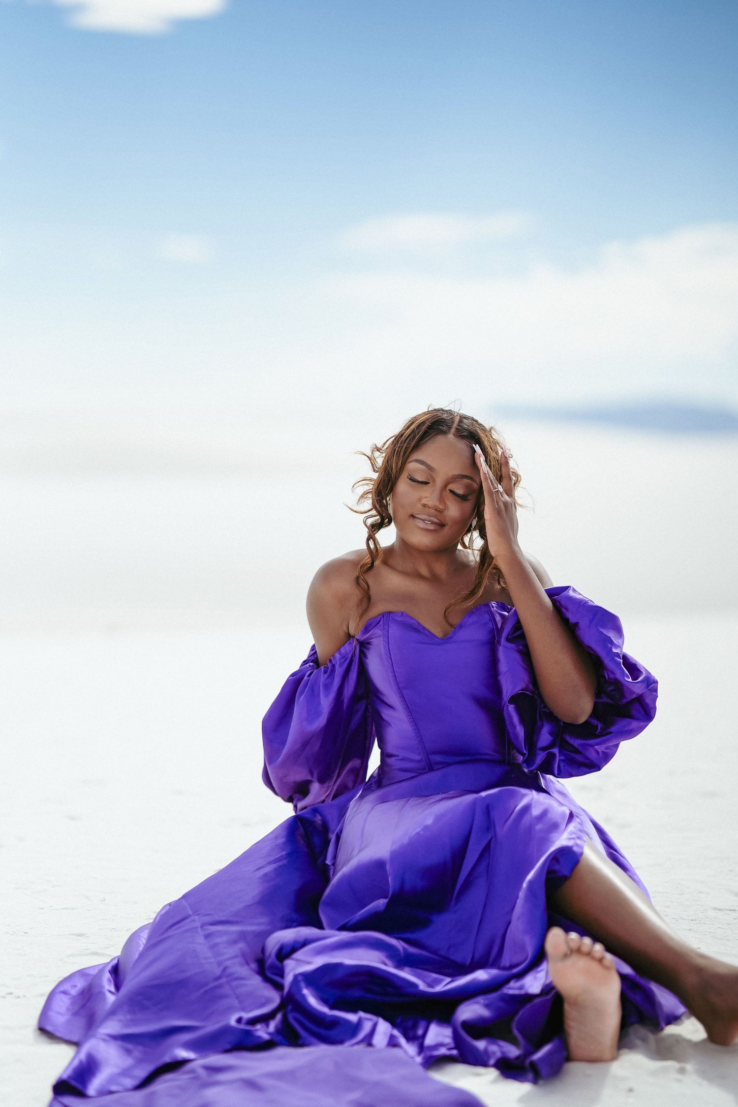 A person in purple dress reclines expressively on white sand during golden hour.