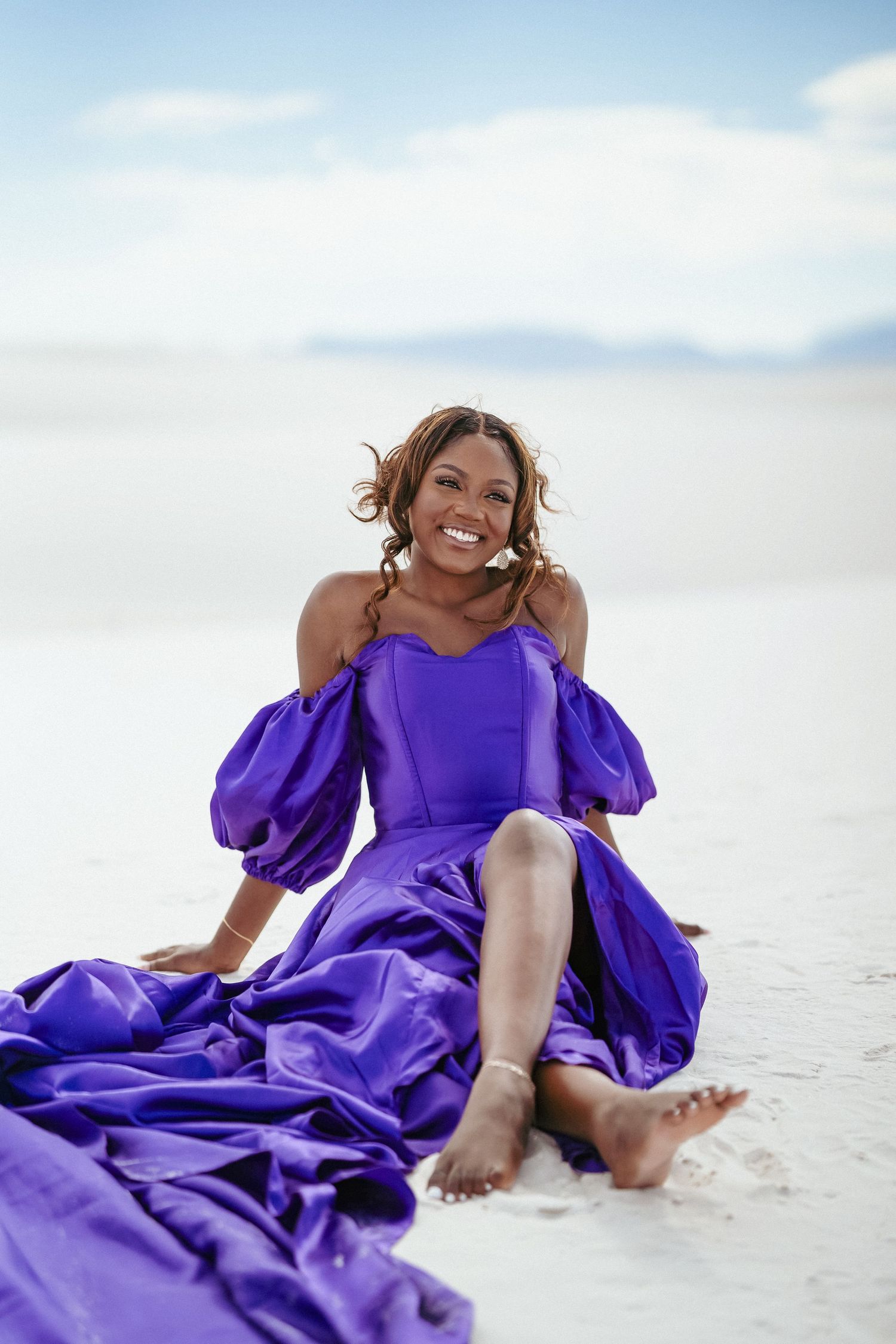A person in purple dress creates joyful poses during beach photo session.