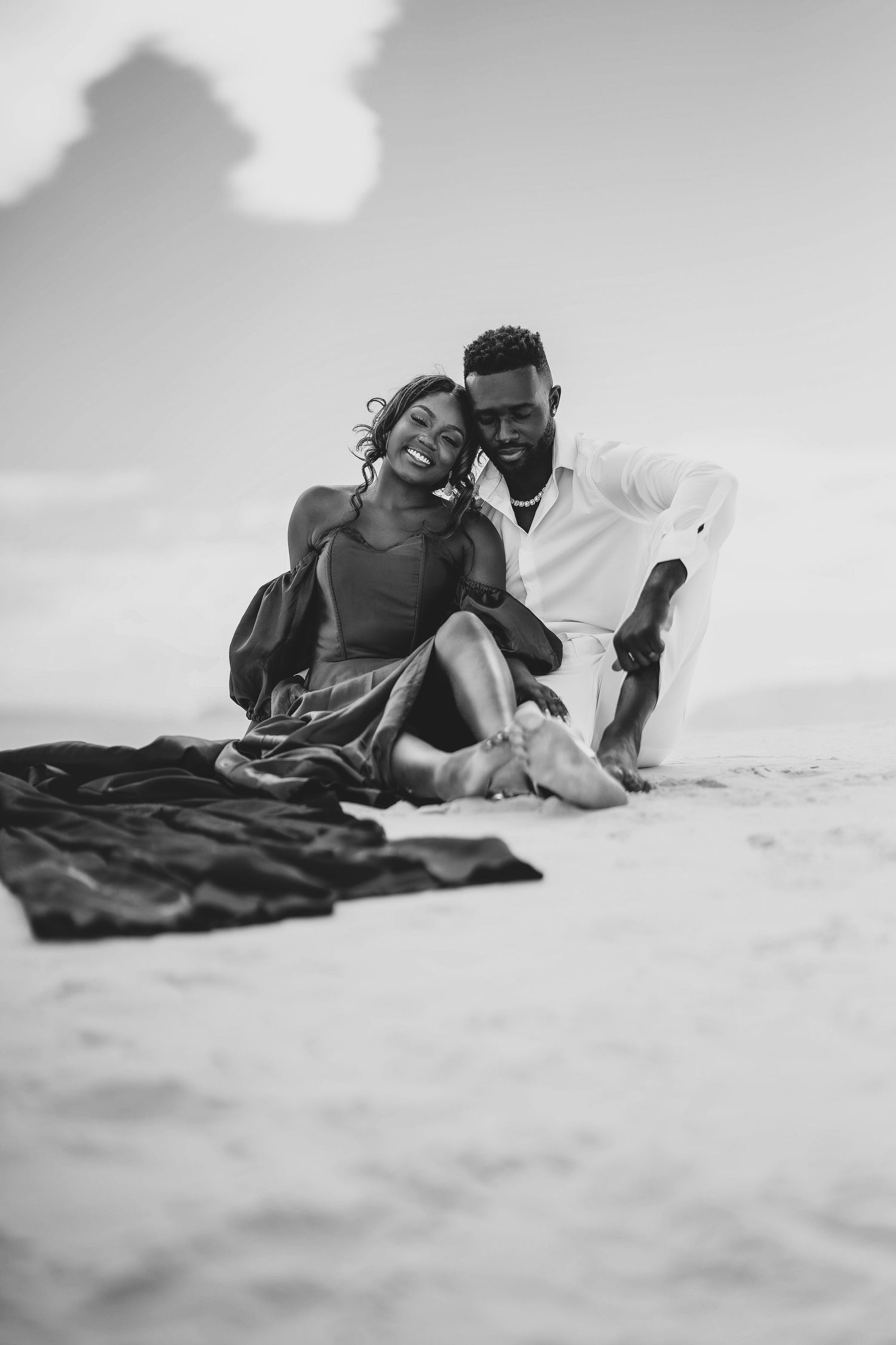A couple shares intimate moments on white sand during black and white photo shoot.