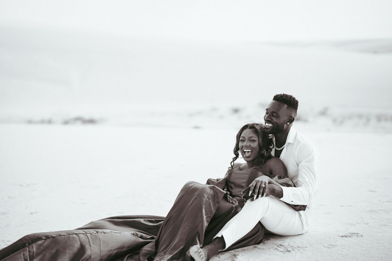 Black and white romantic portrait of couple lying together on sand.
