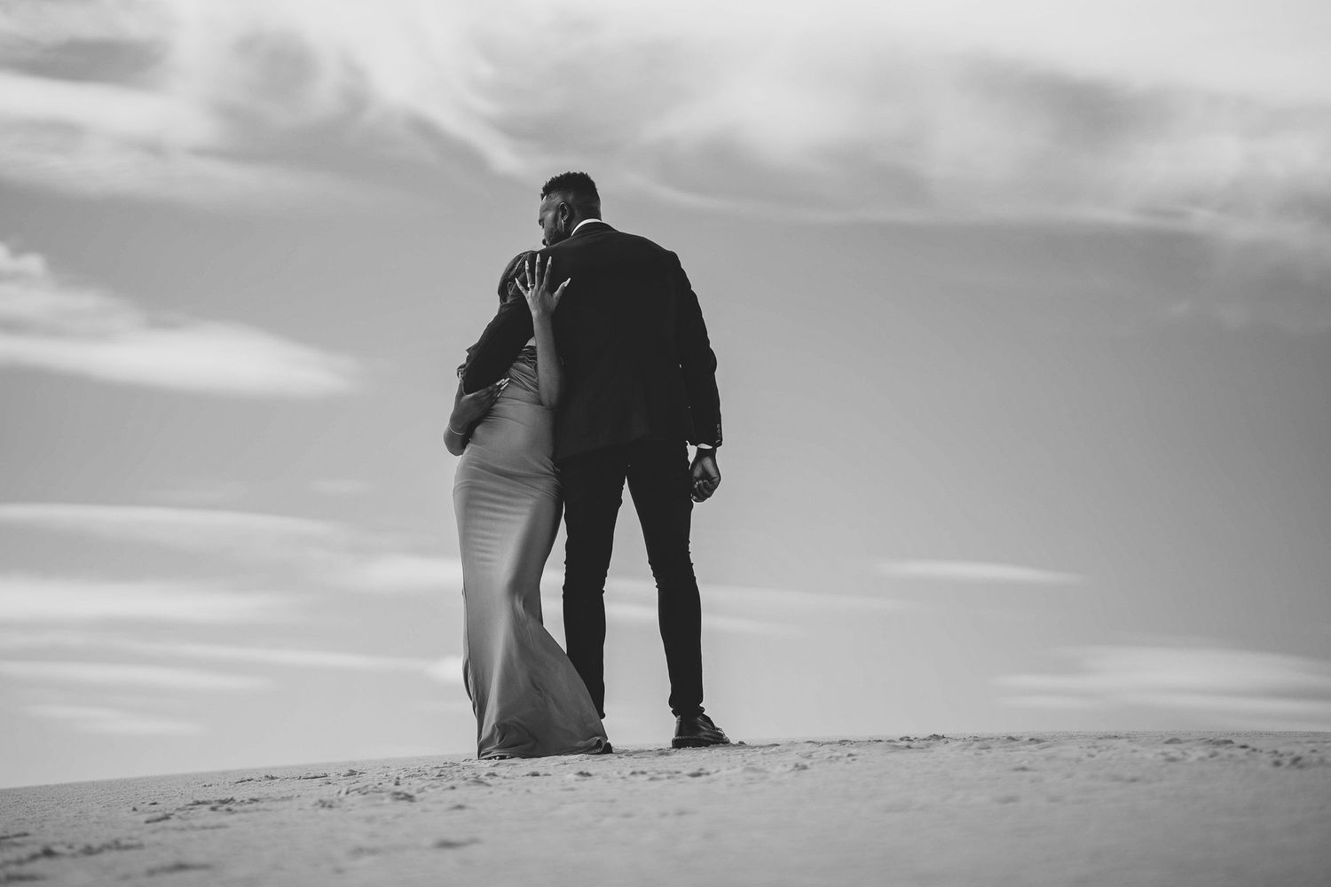 Silhouetted figures stand together on sand dune against cloudy sky.