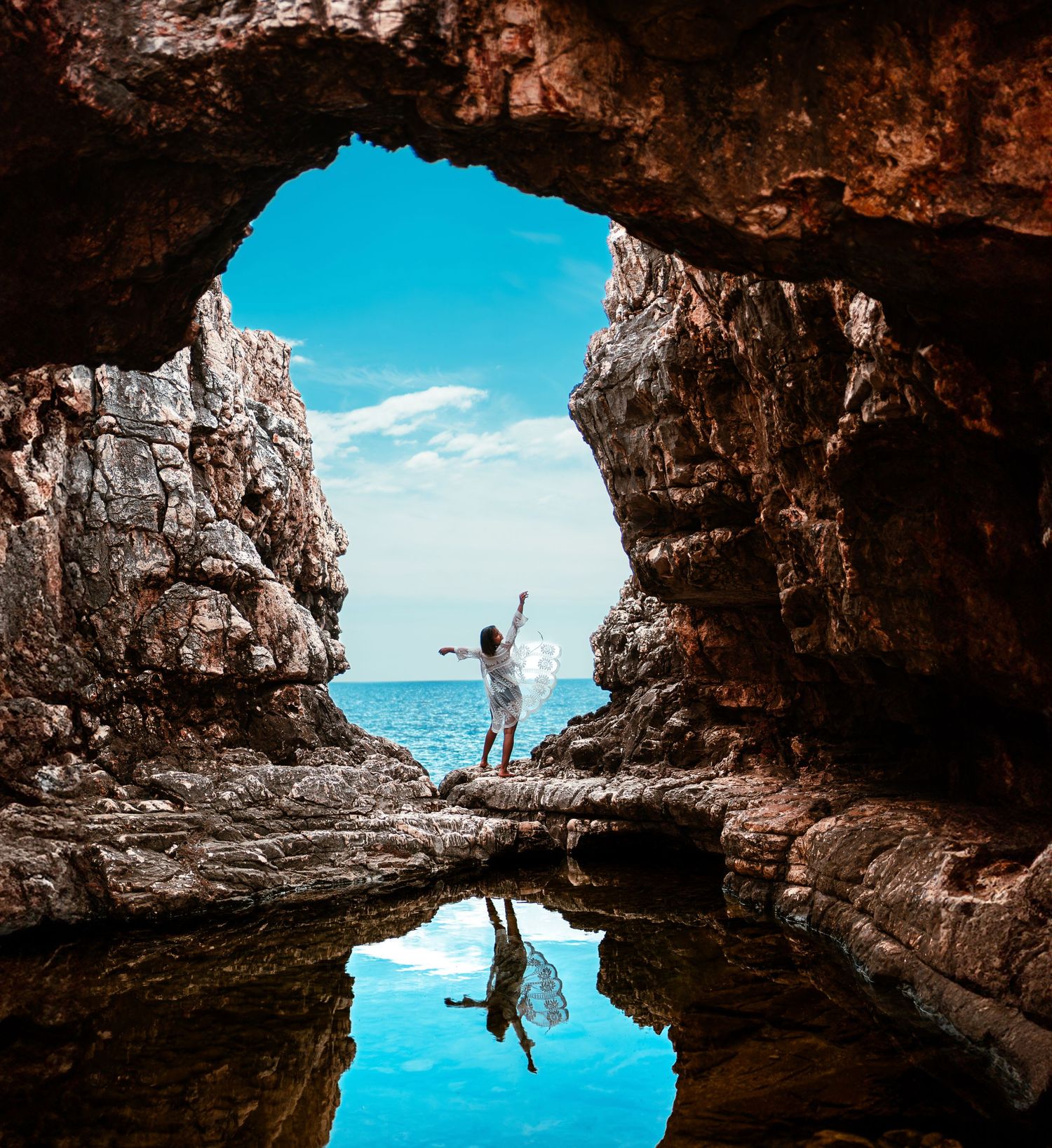 Silhouette of person in cave opening with ocean reflection below.