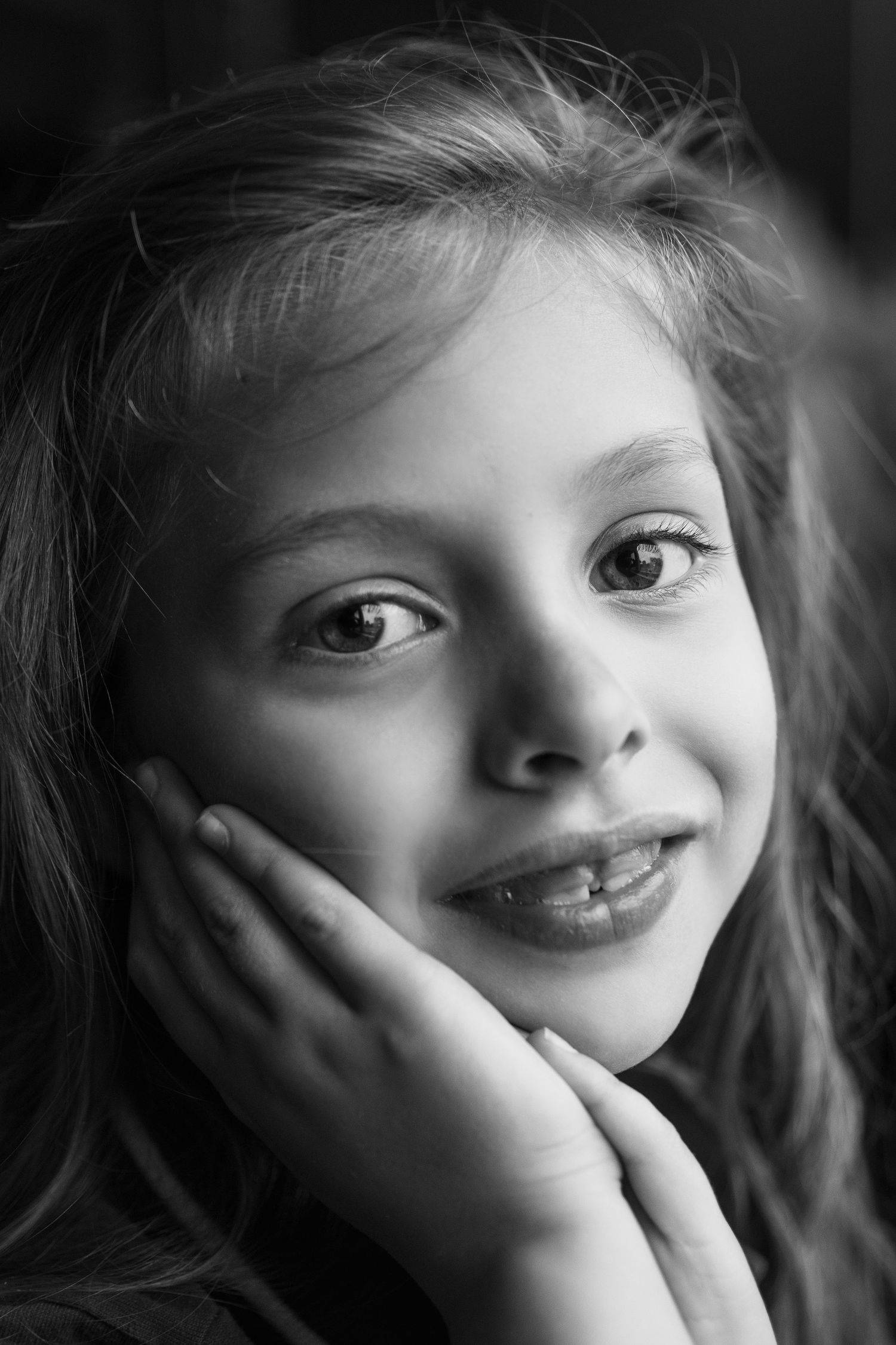Black and white portrait of a young child with a gentle smile resting their chin on their hand.