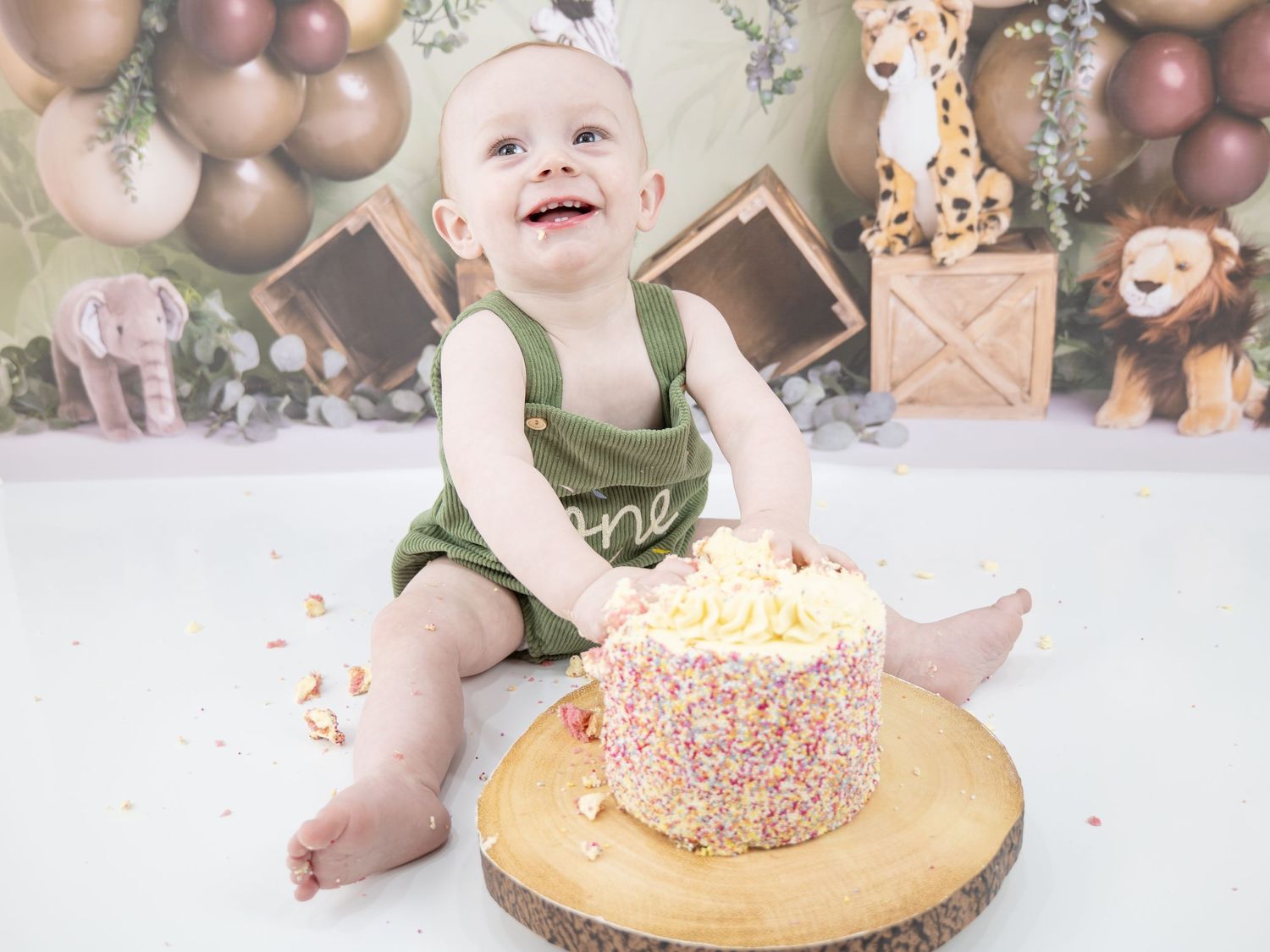 Whimsical cake smash photo setup with neutral balloon arch, eucalyptus leaves, and small dessert on white background.