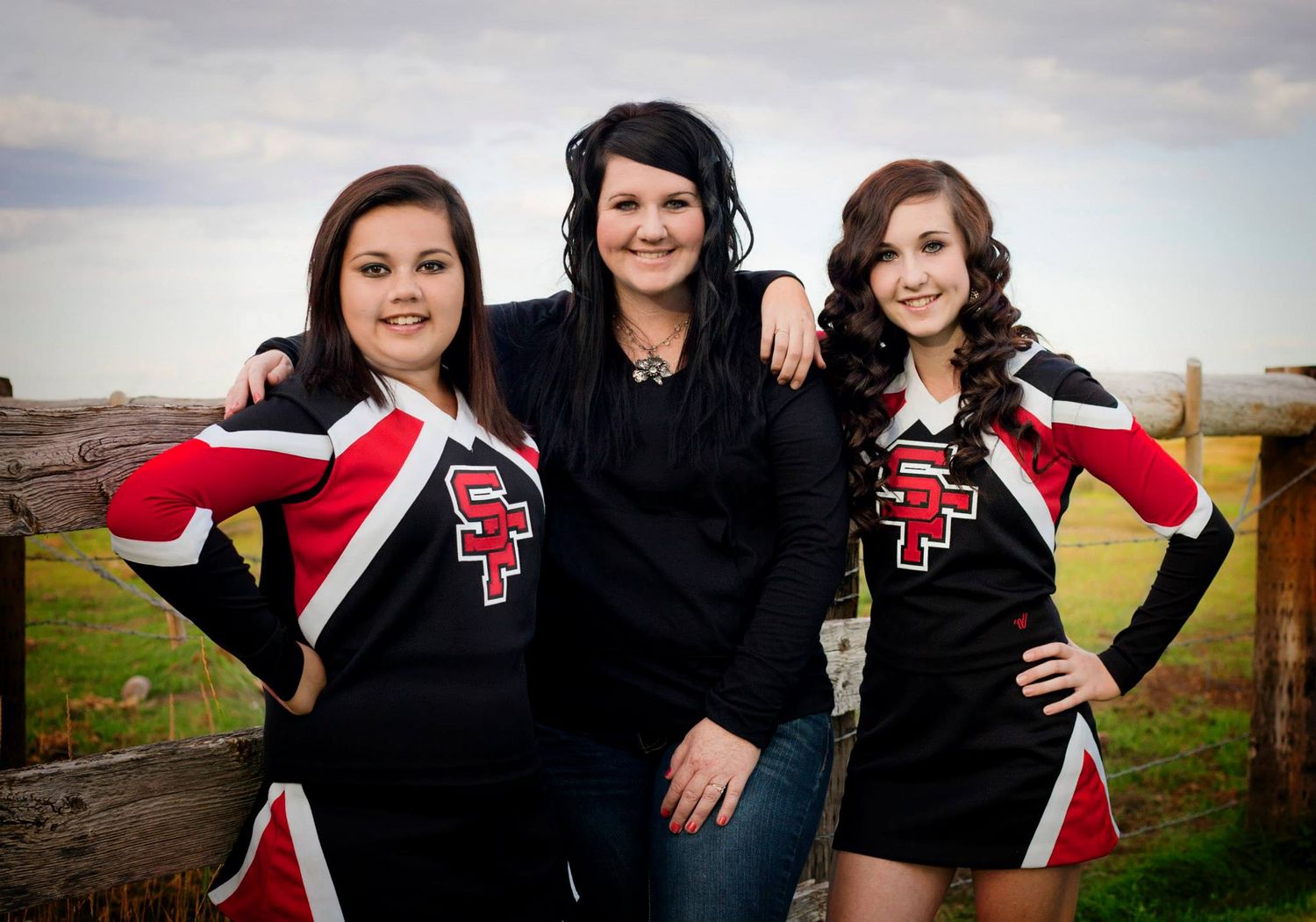 Three cheerleaders pose together wearing black and red uniforms in an outdoor setting.