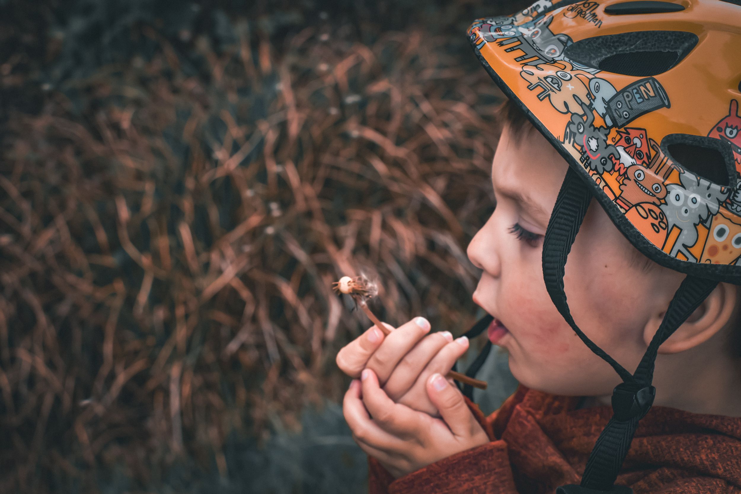 Child in orange helmet chewing on something while wearing winter clothing outdoors.