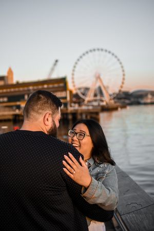 Couple sharing romantic moment at waterfront with Ferris wheel in background at sunset.