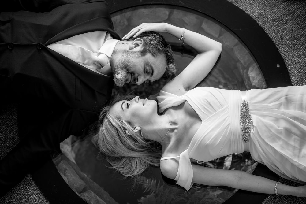 Black and white overhead shot of bride and groom lying down face to face in a romantic wedding portrait.