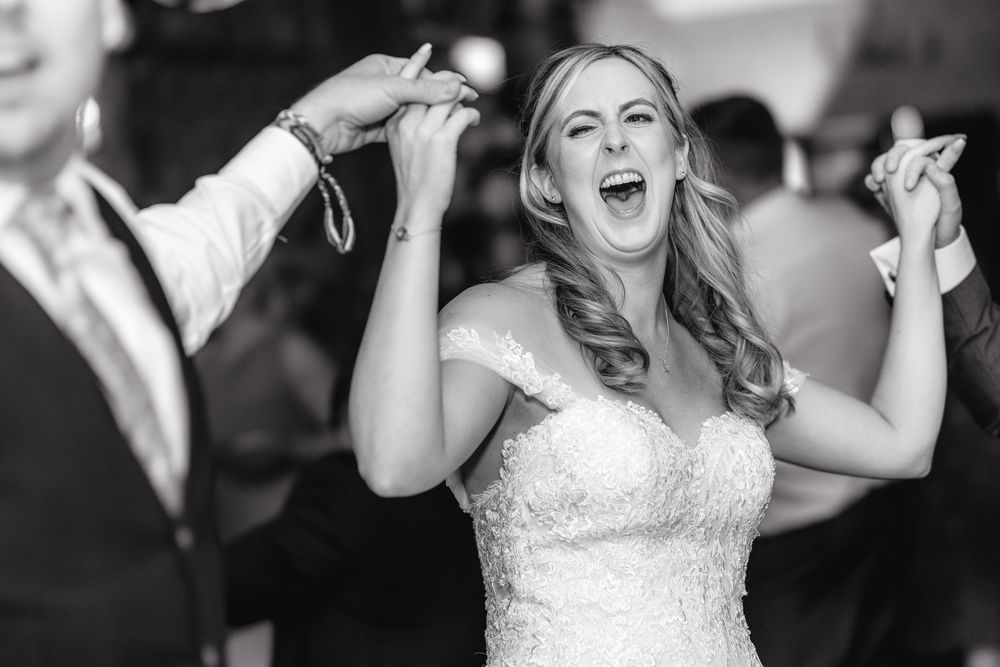 A joyful bride in a white dress laughs and dances during a wedding celebration.