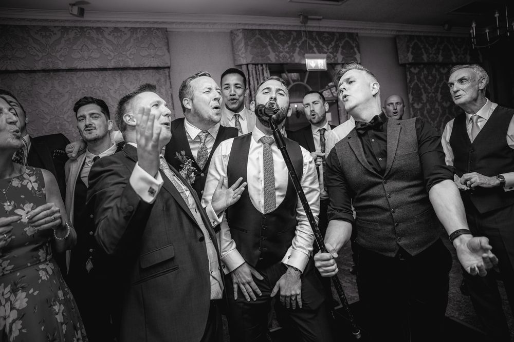 Black and white photo of wedding guests dancing and celebrating together at a reception party.