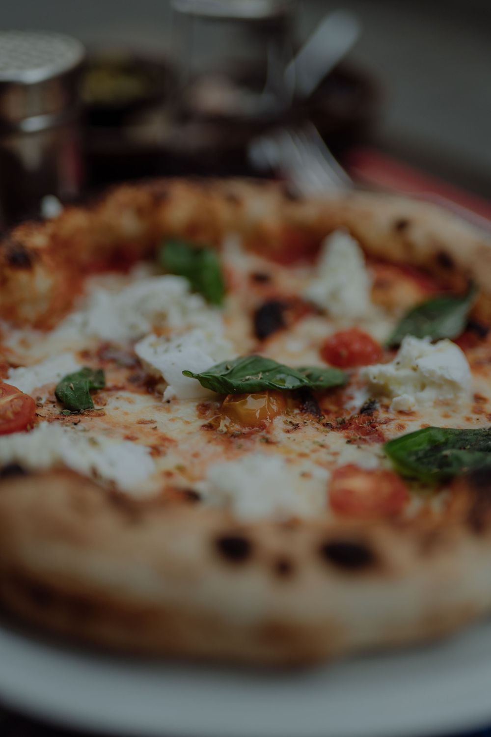Close-up of a Neapolitan pizza with fresh basil, tomatoes and melted mozzarella on a white plate.