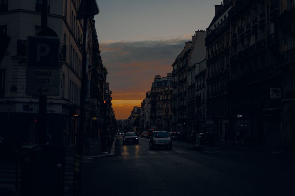 Moody sunset view down a Parisian street with classic Haussmann buildings and car lights.