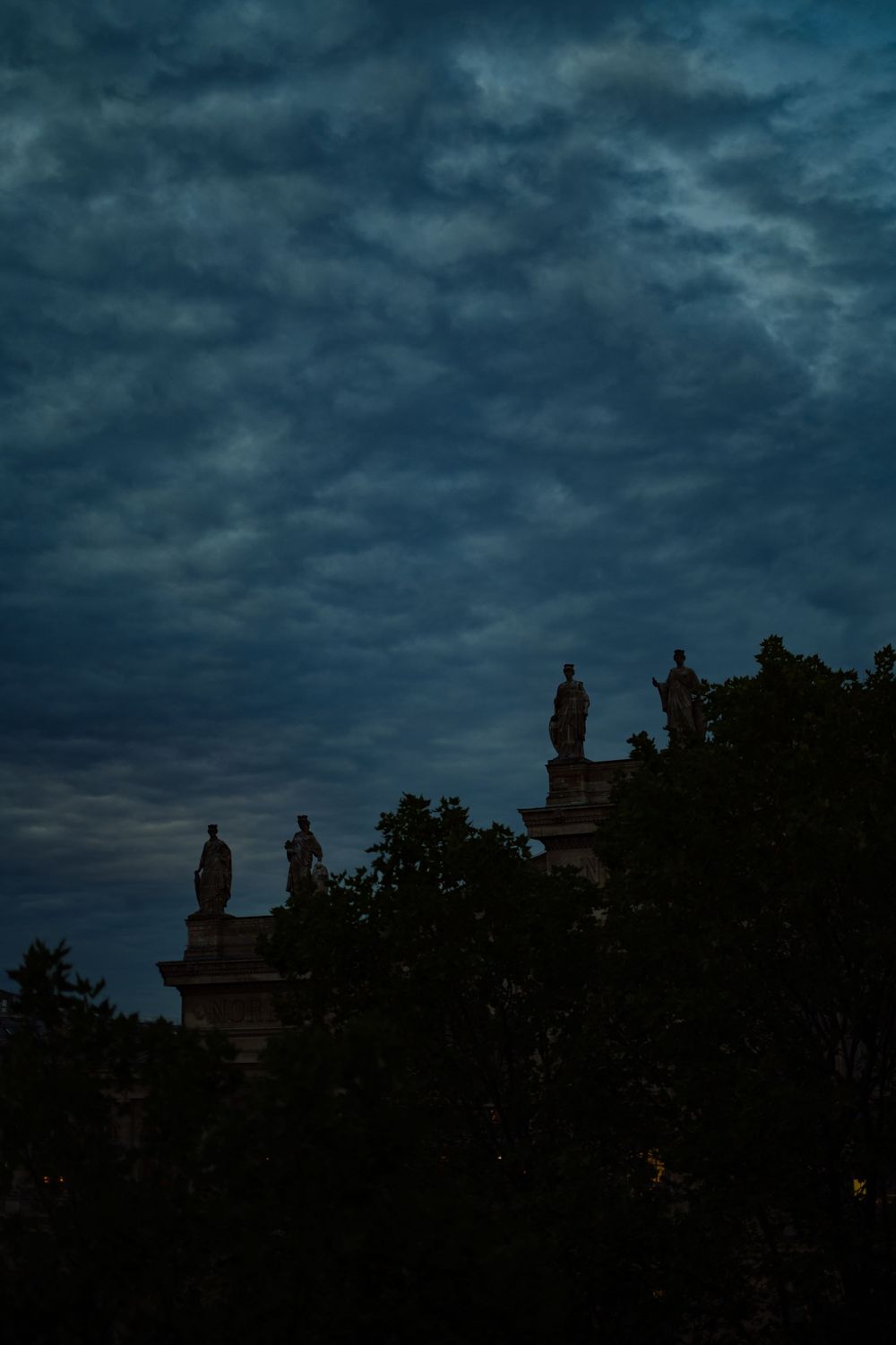 Dark silhouettes of statues against a dramatic stormy blue sky.