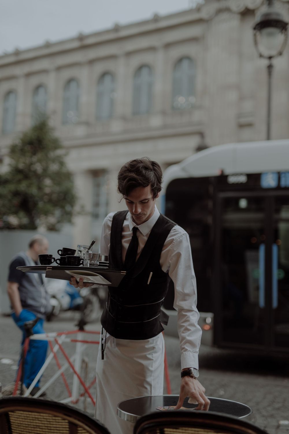 Waiter in formal attire preparing service at an outdoor Parisian cafe.