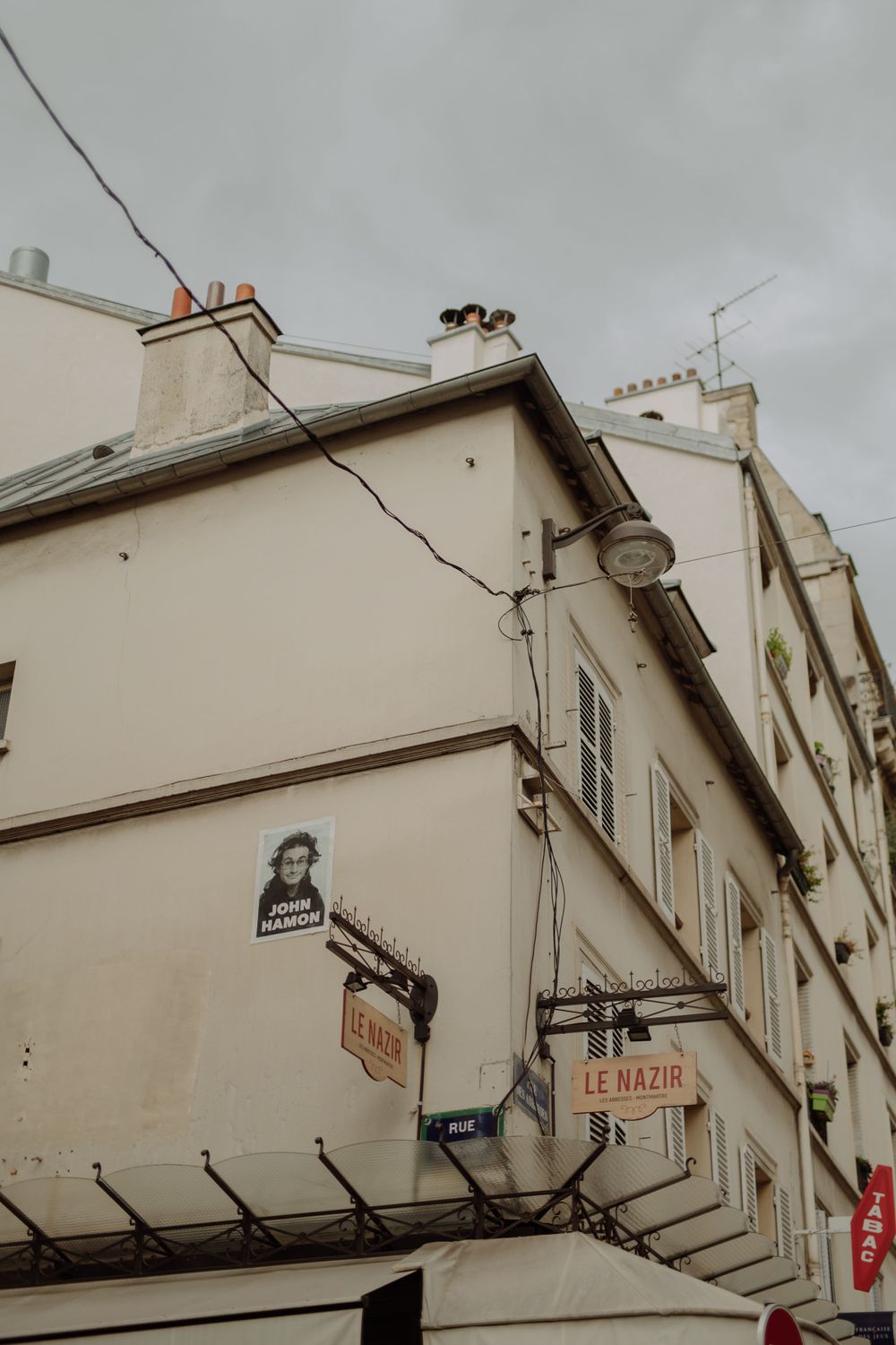 Classic Parisian building facade with street signs and architectural details against an overcast sky.
