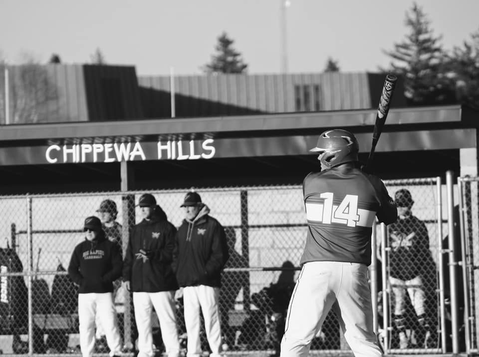 Baseball player #14 batting at Chippewa Hills field in black and white photo with coaches in background.