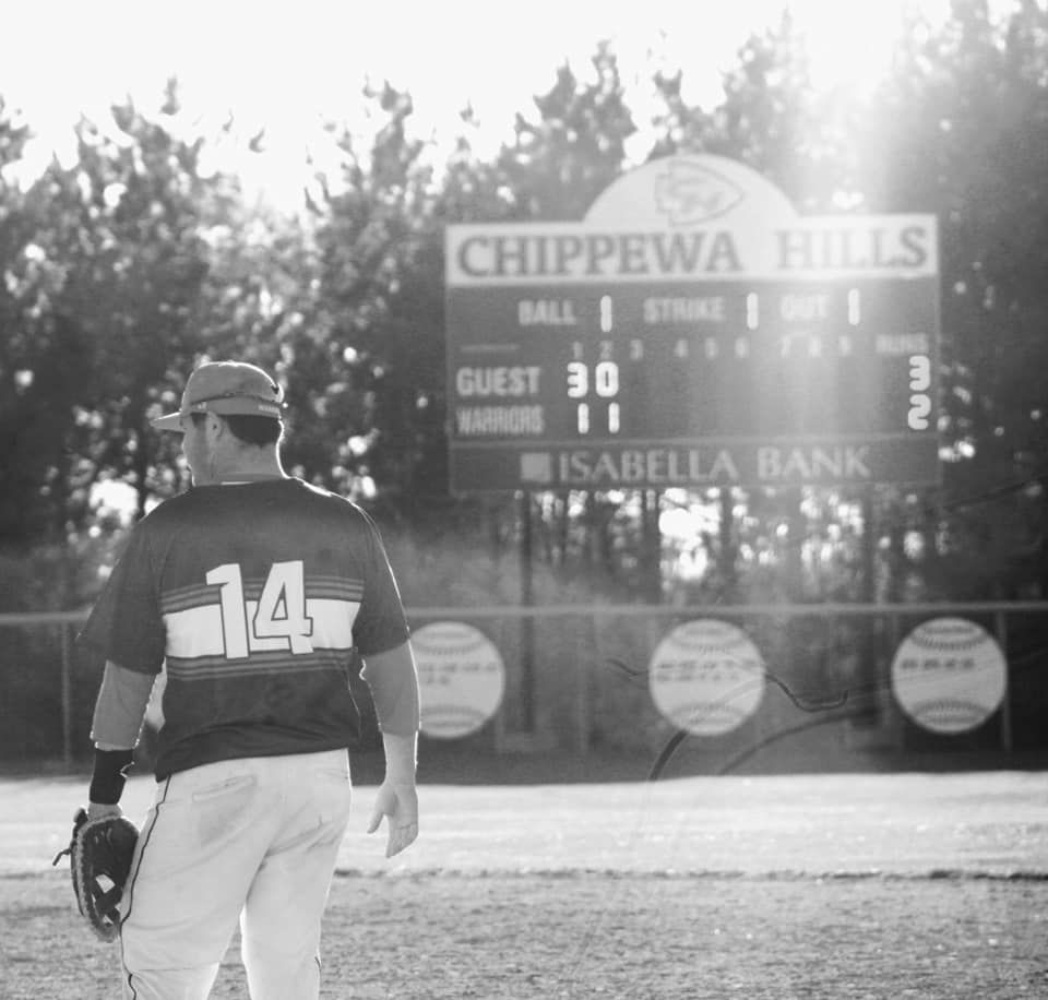 Baseball player #14 stands on field facing Chippewa Hills scoreboard in black and white photo.