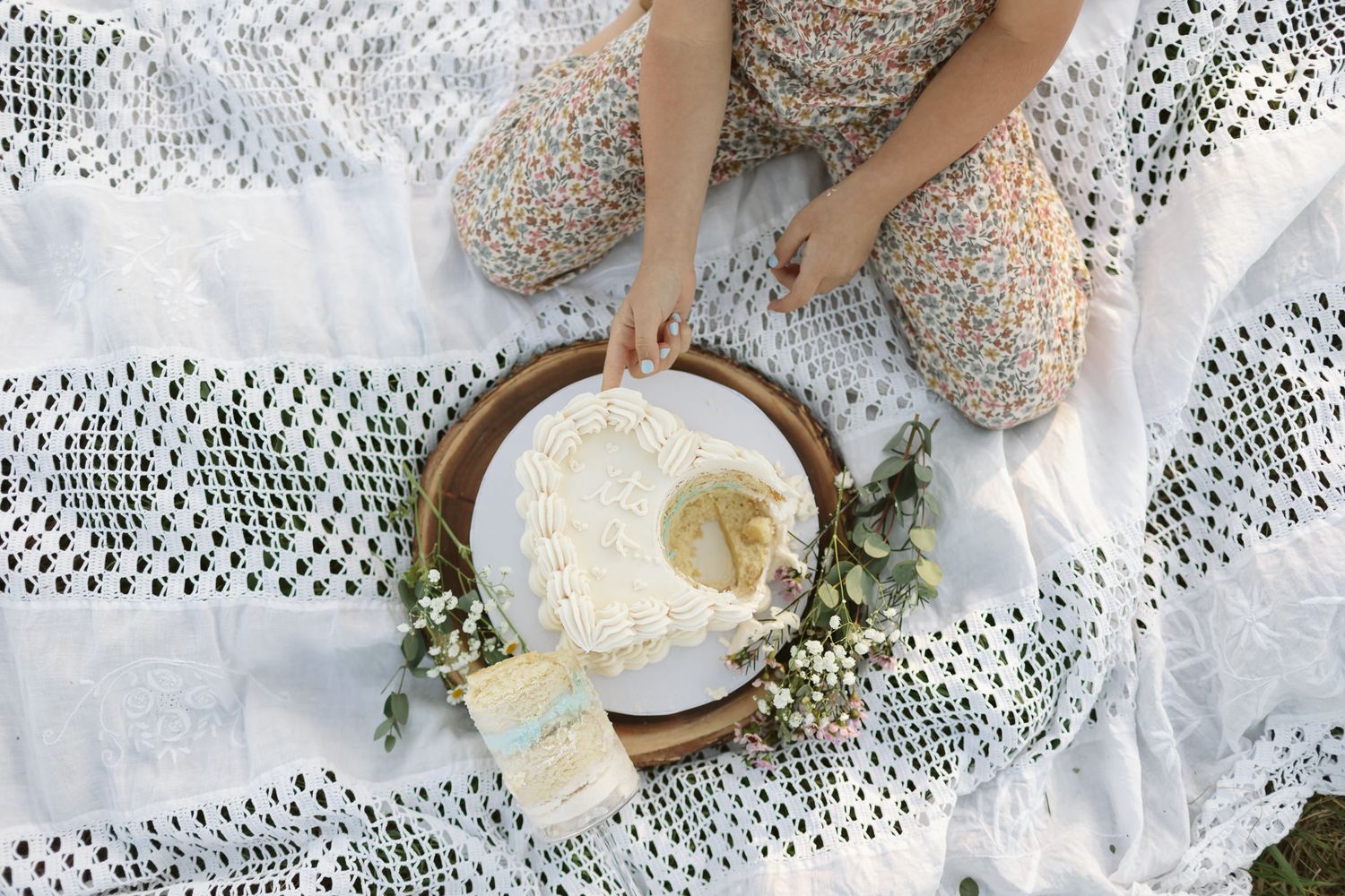 older sister putting finger into side of white gender reveal cake to discover blue frosting indicating baby brother