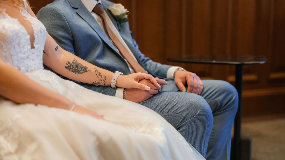 Close-up view of a couple sitting together during their wedding ceremony, showing their hands and formal attire.