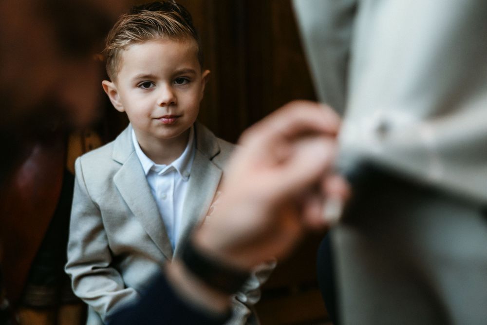 A young child in a light grey suit sits attentively while listening during a formal occasion.