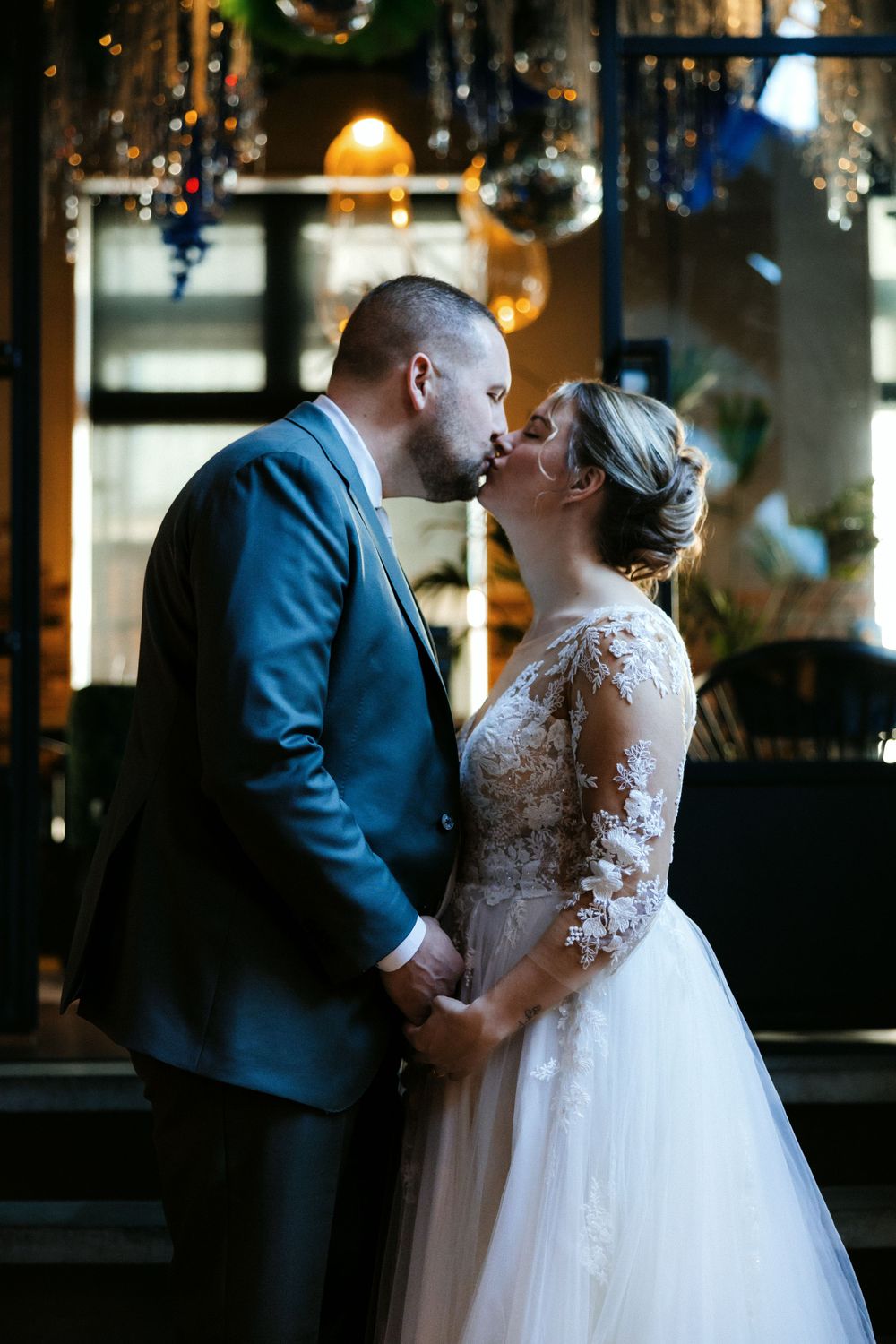 A romantic wedding photograph of a couple sharing an intimate moment under decorative lighting in a dimly lit venue.