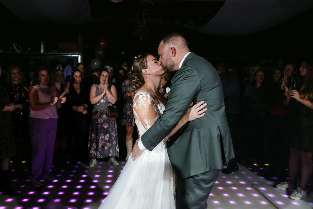 Couple shares intimate first dance on illuminated purple dance floor at wedding reception while guests watch from perimeter.
