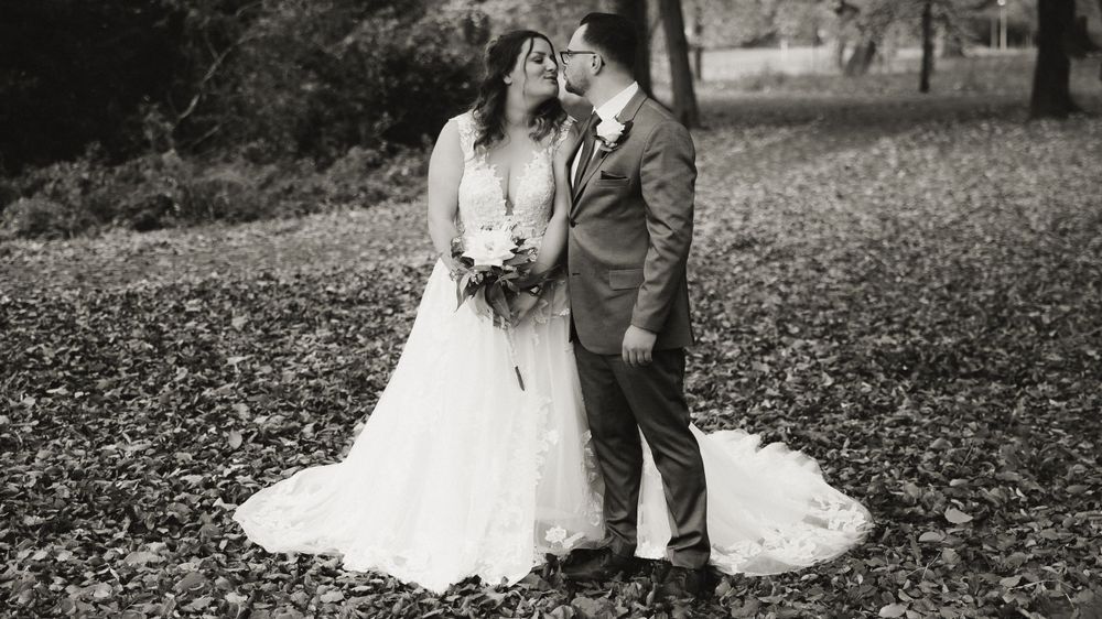 A black and white wedding photograph of a couple standing together on fallen autumn leaves in a park setting.
