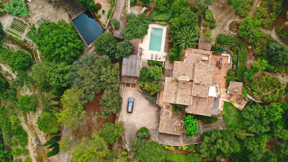 Overhead drone shot of a Mediterranean estate with pool and landscaped grounds amidst green forest.