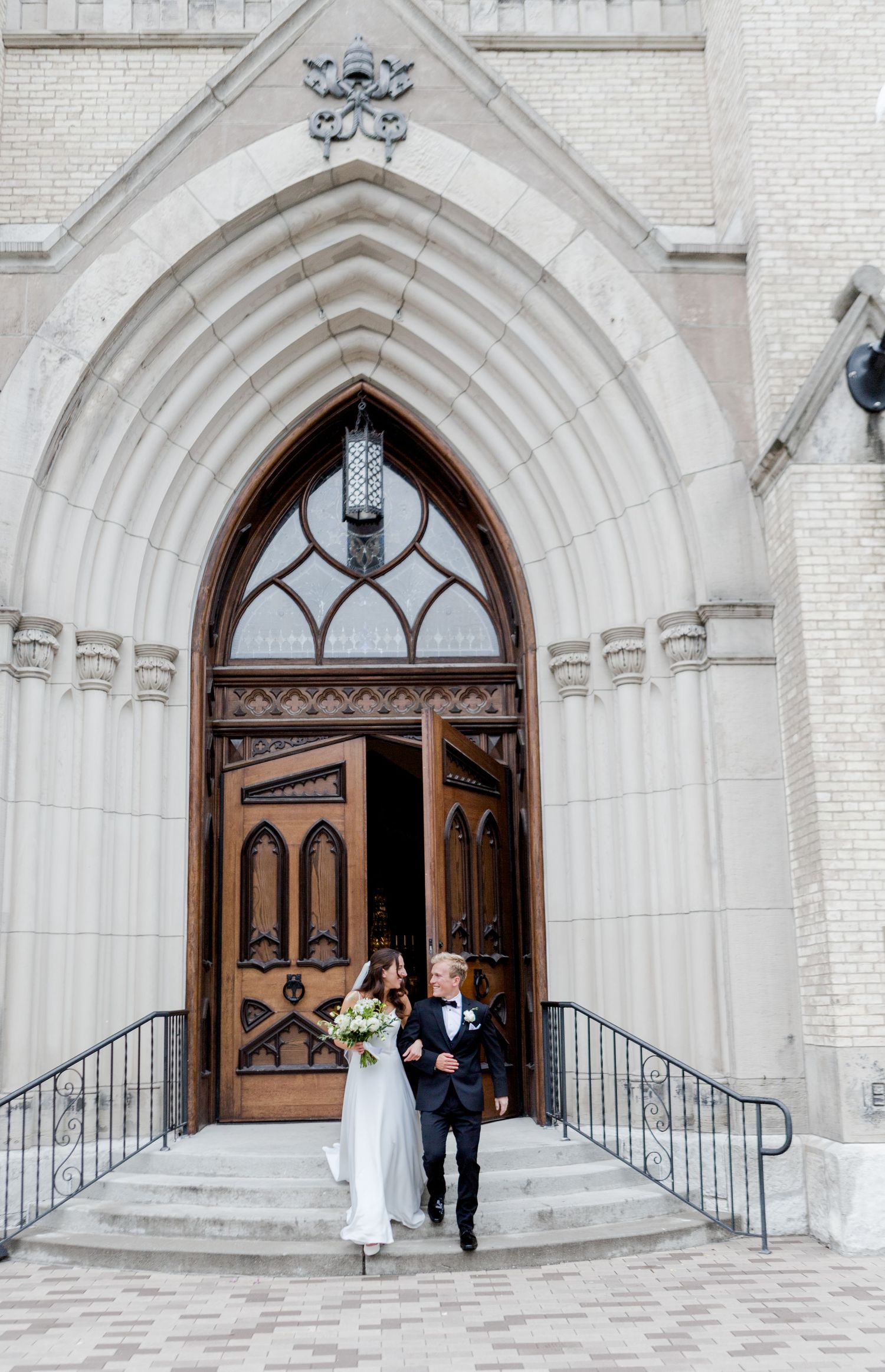 Gothic church entrance with arched wooden doors and white stone facade showing wedding ceremony guests arriving.
