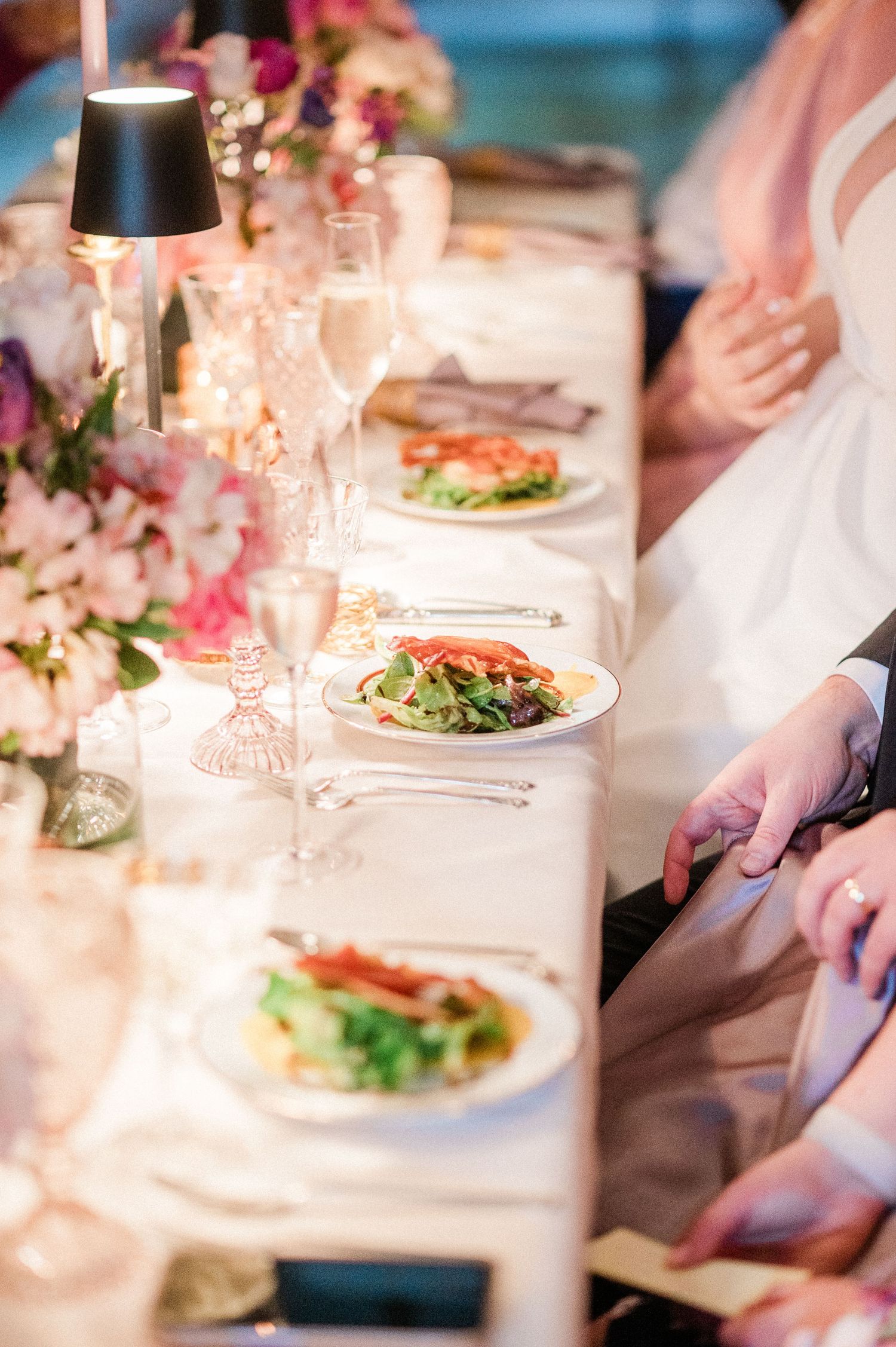 Elegant wedding reception table setting with plated meals and pink floral decorations.