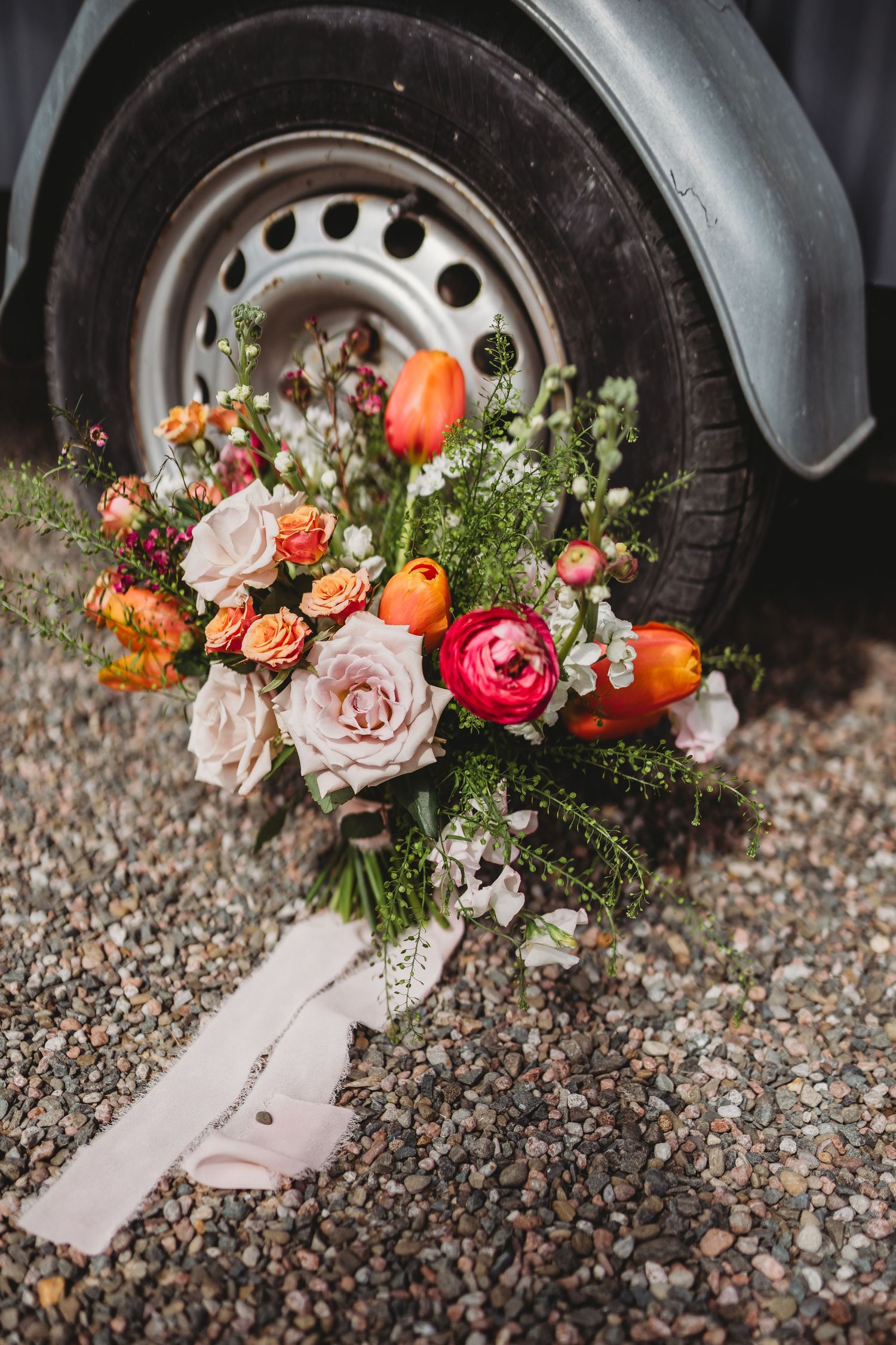 Colorful wedding bouquet with roses and tulips resting against a vintage car wheel.