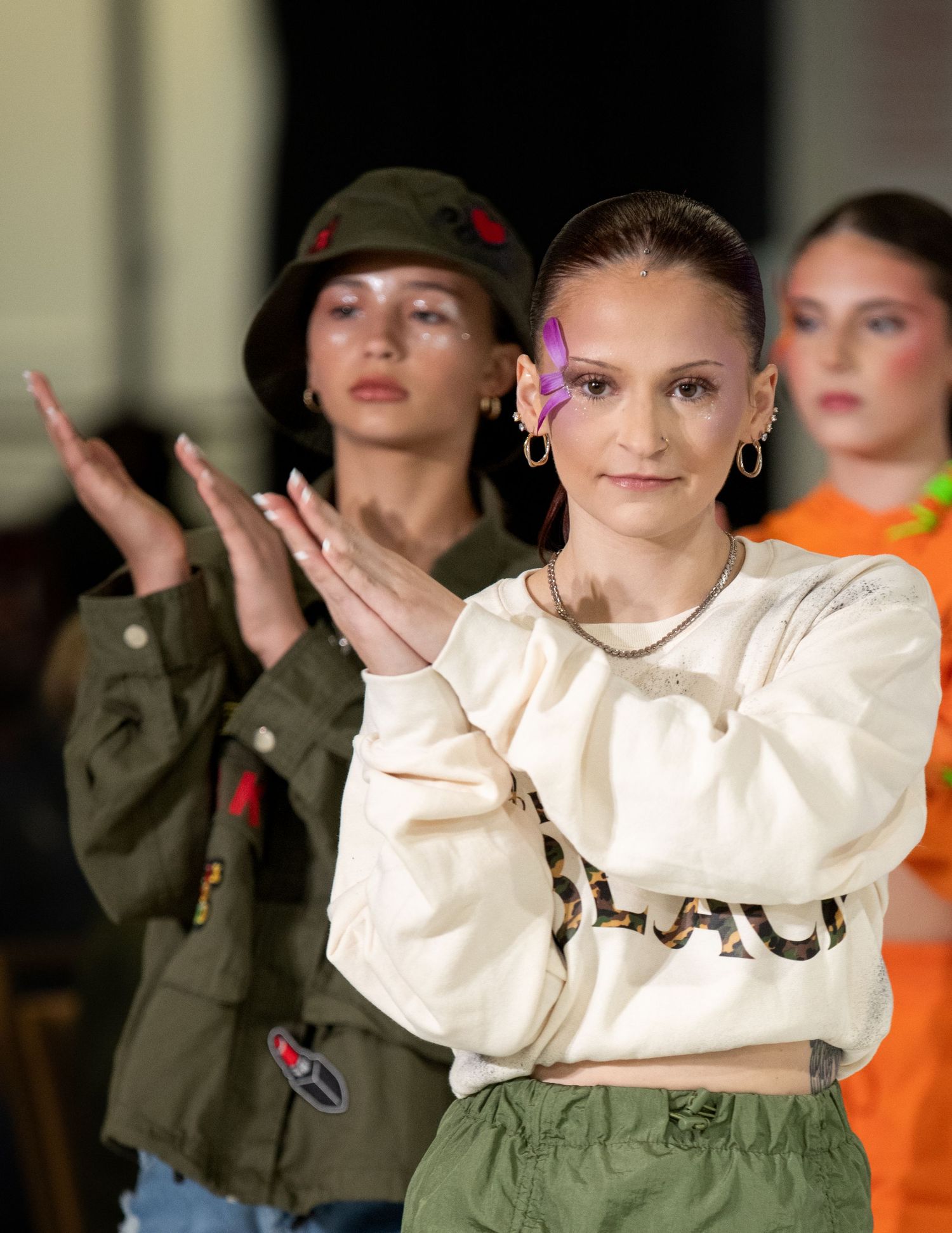 Fashion show features casual streetwear looks with military jacket and cream sweatshirt styling.