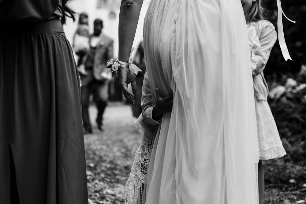 Black and white detail shot of wedding guests and bride's dress at outdoor ceremony.