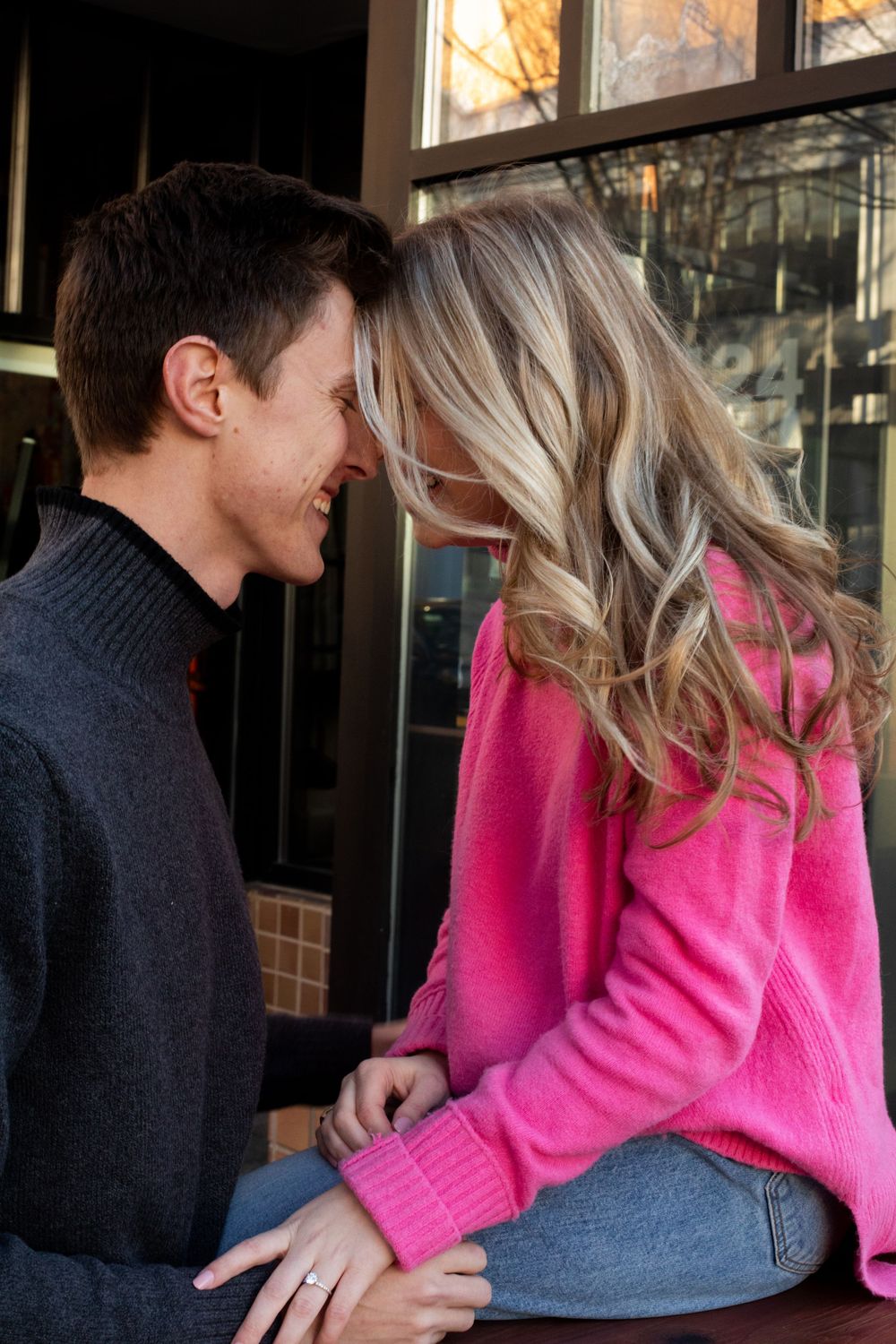 Intimate couple's photoshoot with bright pink sweater against storefront windows.