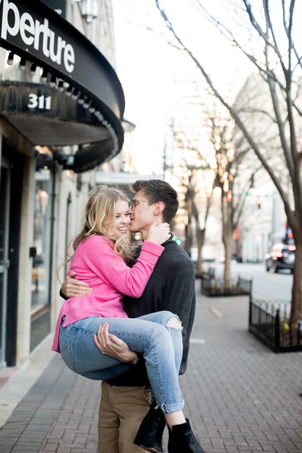 Romantic couple embracing on an urban sidewalk with storefronts.
