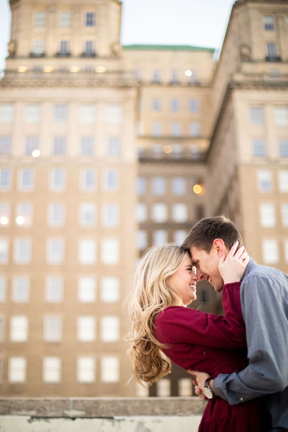 Couple in burgundy and grey sharing tender moments against historic building backdrop.