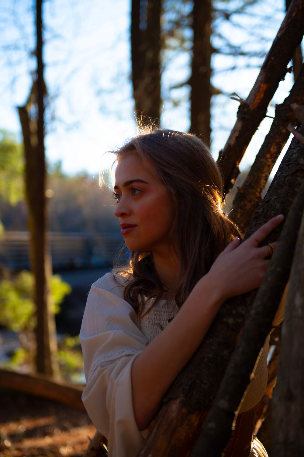 A dreamy portrait in warm light shows a person leaning against trees in a forest setting.